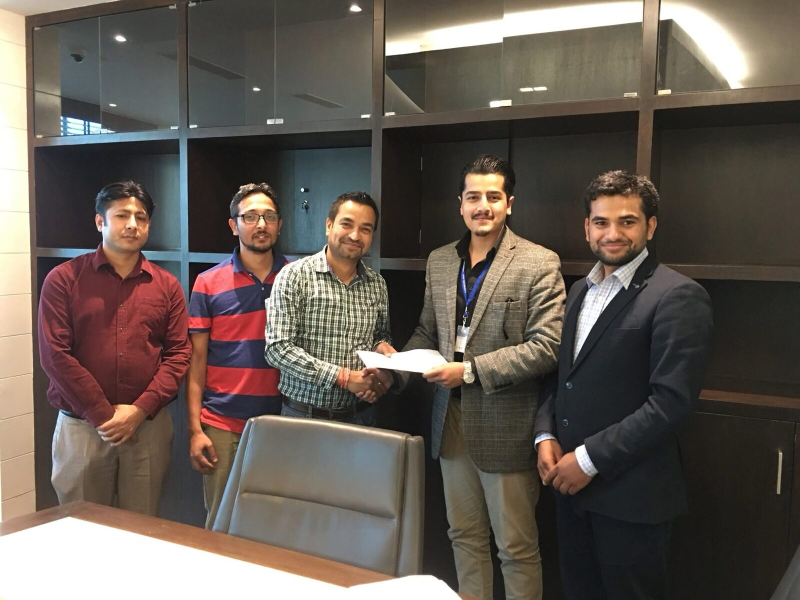 Five people in a boardroom; a cheque is handed to a founder across a handshake.