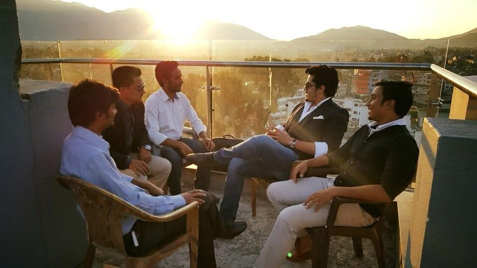 Five colleagues sitting in a circle on a Kathmandu rooftop at sunset, hills in the background.