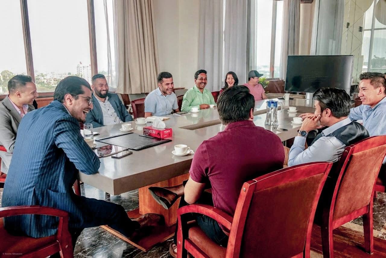 Twelve people around a boardroom table in conversation, windows overlooking Kathmandu.